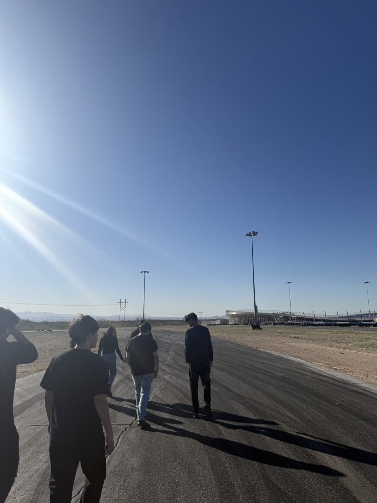 A group of students walking along a race track, silhouetted against the sun.