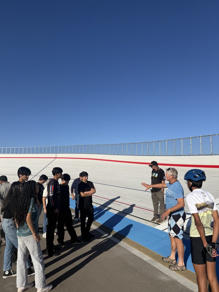 A group of students gathered along a steeply curved race track. 