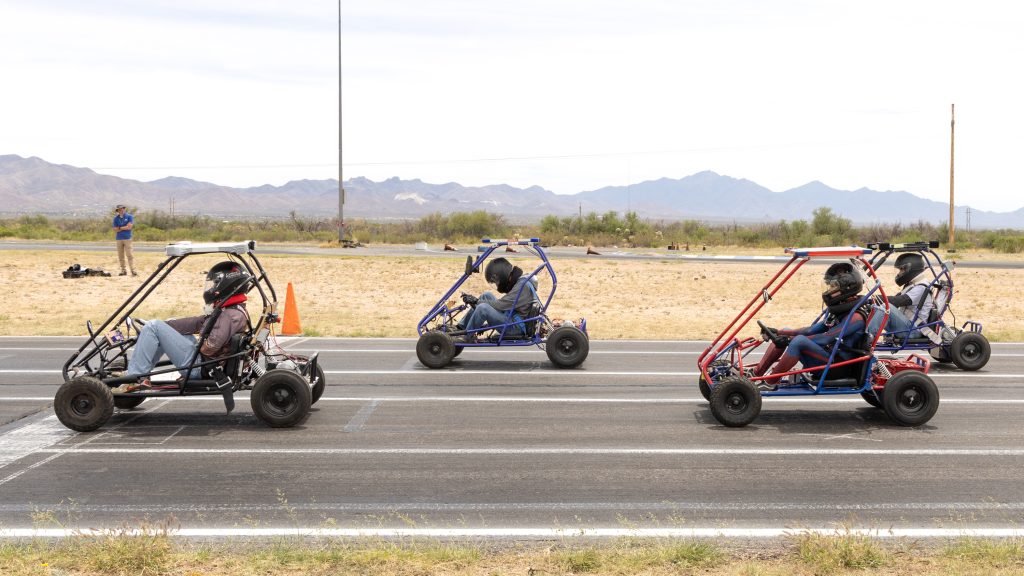 Four solar-powered go-karts on a paved track with a mountainous backdrop.